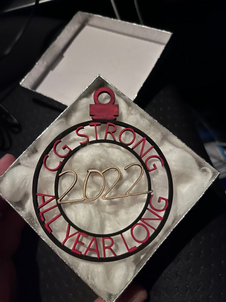 One of a kind Custom ornament made of thin wood. The inner circle has the year listed horizontally within a thin circle. between that circle and an outter circle the words curve along the line. The top reads "CG Strong" and the bottom reads "all year long"