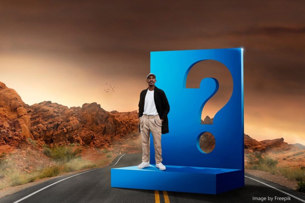 Do you have questions? image features a guy standing on platform next to large question mark which is placed in the road of a desert scene at dusk. 